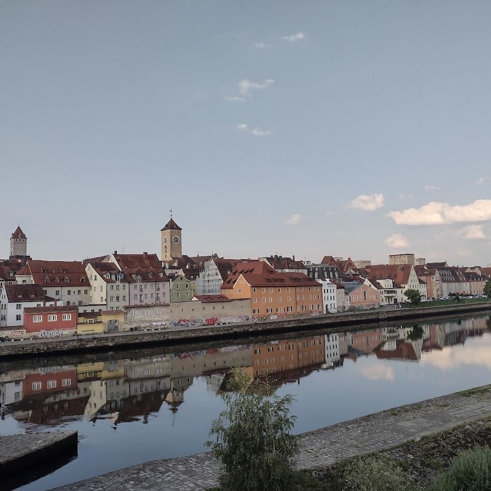 A riverfront town with a clock tower. The town is reflected in the water. This is in Landshut, Germany.